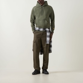 Model wearing Carhartt Chase Logo Hoodie in Leaf/Gold with olive cargo trousers and a plaid shirt tied at the waist, black chunky trainers.