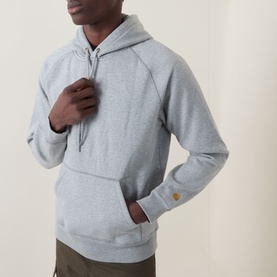 Model wearing Carhartt Chase Logo Hoodie in grey heather, showing gold embroidered sleeve logo, kangaroo pocket and adjustable drawstring hood.