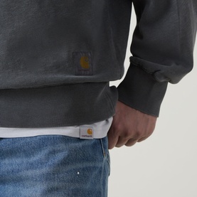 Model wearing Carhartt Harper Logo Half-Zip Sweatshirt in Black, close-up showing logo badge detail, styled with white tee and blue jeans.