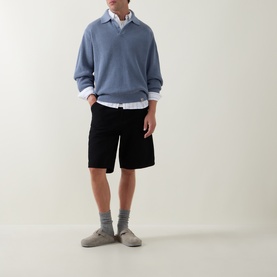 Model wearing Carhartt Shady Blue cotton polo knit, styled with white shirt, black shorts, grey socks and slip-on shoes.