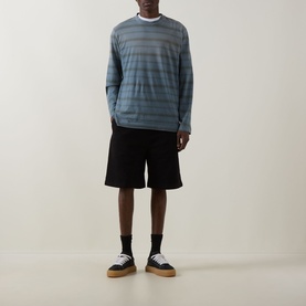Model wearing Carhartt black cotton shorts with elastane, styled with a blue striped long-sleeve top and cream sole trainers.