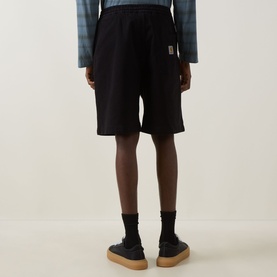 Model wearing Carhartt black cotton shorts with elasticated waist and small logo patch, styled with blue shirt and tan shoes.