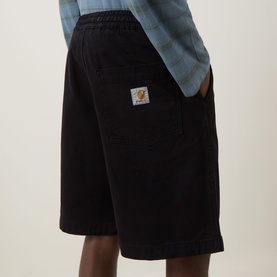 Model wearing Carhartt black cotton shorts with elasticated waist, patch logo detail, and side pocket, styled with a blue shirt.