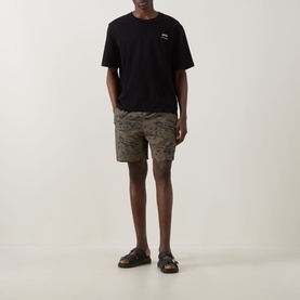 Model wearing Carhartt shorts in Duck Feather camo print, styled with a black T-shirt and dark leather loafers.