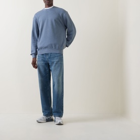 Model wearing Carhartt Landon Tapered Leg Jeans in Blue, loose tapered fit with destroyed wash, styled with blue sweatshirt and grey trainers