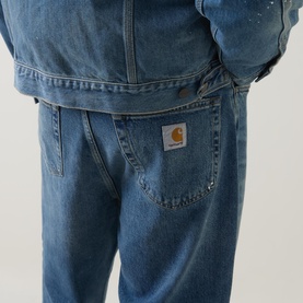 Model wearing Carhartt Landon Tapered Leg Jeans in blue, showing back pockets with woven logo badge, paired with denim jacket
