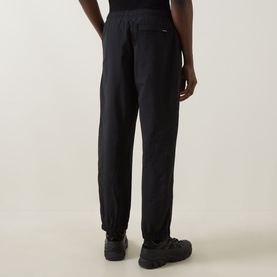 Model wearing Carhartt Travon Script Logo Track Pants in Black, shown from behind with cuffed ankles and straight-leg fit, styled with chunky