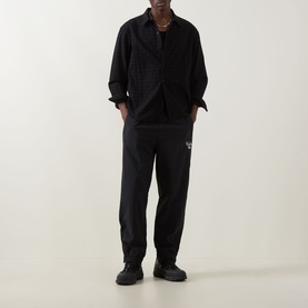 Model wearing Carhartt Travon Script Logo Track Pants in Black, styled with matching black overshirt and black trainers.