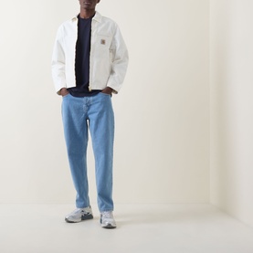 Model wearing Carhartt Newel Tapered Leg Jeans in blue, styled with a white jacket, navy tee and grey trainers.