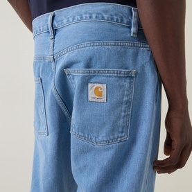 Model wearing Carhartt Newel Tapered Leg Jeans in blue, close-up of back pocket with woven logo badge, relaxed tapered fit, 100% cotton denim