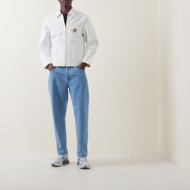Model wearing Carhartt Newel Tapered Leg Jeans in blue, styled with a white zip jacket and grey trainers.