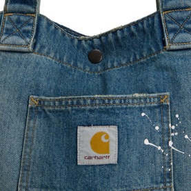 Carhartt denim tote bag in blue, close-up showing chest pocket with logo patch, snap fastening, and paint splatter detail