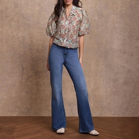 Model wearing Mint Velvet red floral puff-sleeve blouse, styled with mid-blue flare jeans and cream heeled mules