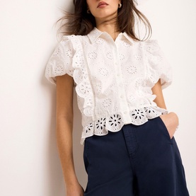 Model wearing Mint Velvet white broderie anglaise blouse with puff sleeves and ruffle hem, styled with navy wide-leg trousers