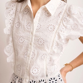 Model wearing Mint Velvet white broderie anglaise top with floral cutwork detail, ruffle trim and button front, styled with gold bracelet