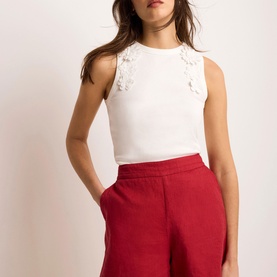 Model wearing Mint Velvet white sleeveless top with floral lace shoulder detail, styled with red wide-leg shorts.