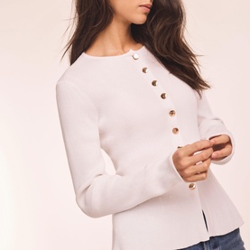 Model wearing Mint Velvet white knit top with gold button detail along front placket and long sleeves.