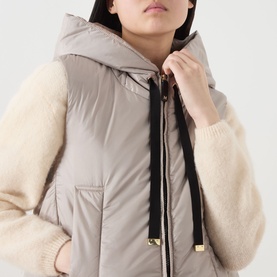Model wearing Max Mara Cube Greengo Padded Gilet in beige with hood and black adjustable drawstring, styled over a cream knit sweater.