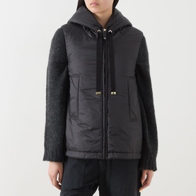 Model wearing Max Mara Cube black quilted gilet with hood, styled with matching black chunky knit sleeves and gold-tone hardware detail.