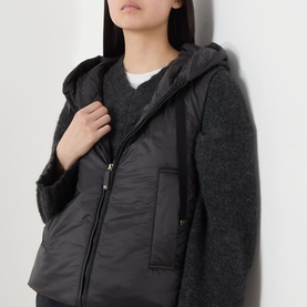 Model wearing Max Mara Cube black quilted polyester gilet with hood, styled over a grey knit sweater