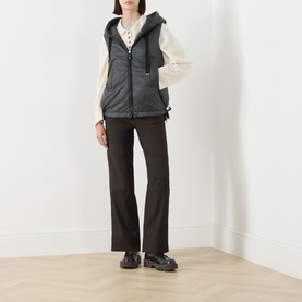 Model wearing Max Mara Cube green quilted gilet with hood, styled with cream knit, dark flared trousers and chunky black shoes.