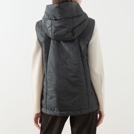 Model wearing Max Mara Cube green quilted hooded gilet, styled with a cream knit jumper and dark trousers, seen from behind.