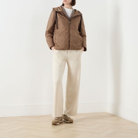 Model wearing Max Mara Cube honey quilted hooded jacket with camel wool blend fill, styled with cream wide-leg trousers and khaki trainers.