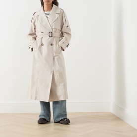 Model wearing Max Mara Cube Coro Trench Coat in silver, double-breasted with belt. Styled with striped top and wide-leg jeans.