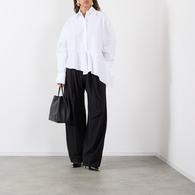 Model wearing Max Mara Sportmax Arcella Asymmetric Optical White shirt with flounce hem, styled with wide-leg black trousers and heels.