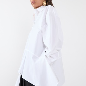 Model wearing Max Mara Sportmax Arcella Asymmetric Shirt in Optical White, showing flounce hem and deep side slit, styled with black skirt