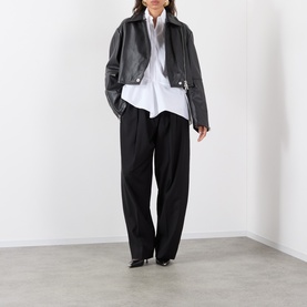 Model wearing Max Mara Sportmax Arcella Asymmetric Shirt in Optical White with asymmetric hem, styled with black leather jacket and wide-leg trousers.
