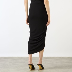Model wearing Max Mara Sportmax black midi skirt in ruched asymmetric hem design, styled with gold-heeled mule sandals, rear view.