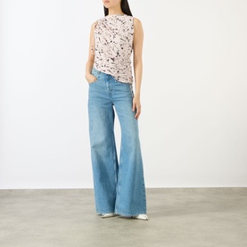 Model wearing Max Mara Sportmax Antique Rose sleeveless printed top with wide-leg blue denim jeans and white shoes.