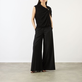Model wearing Max Mara Sportmax black sleeveless draped top with ring detail, styled with wide-leg black trousers and brown sandals.