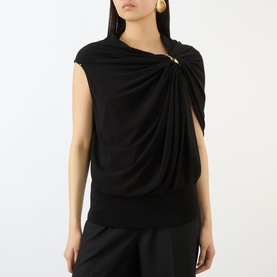 Model wearing Max Mara Sportmax black draped sleeveless top with gold pin detail and asymmetric neckline, styled with black wide-leg trousers.