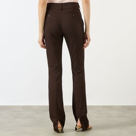 Model wearing Max Mara Sportmax cocoa brown bootcut trousers with rear pockets and split hem detail, paired with heeled mules.