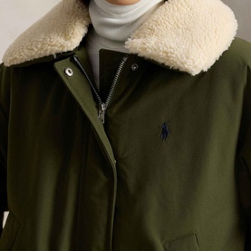 Model wearing Polo Ralph Lauren New Olive coat with cream shearling collar, navy embroidered logo, styled with grey roll-neck underneath.