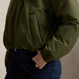 Model wearing Polo Ralph Lauren New Olive padded coat, close-up of side pocket and elasticated cuff detail, styled with dark jeans