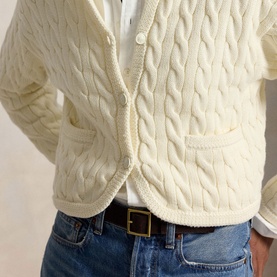 Model wearing Polo Ralph Lauren Clubhouse Cream cable-knit cardigan with patch pockets, styled with white shirt and blue jeans.