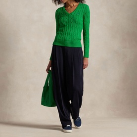 Model wearing Polo Ralph Lauren Preppy Green cable-knit V-neck jumper, styled with navy wide-leg trousers, navy trainers, and green tote bag.