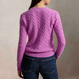 Model wearing Polo Ralph Lauren Pony Logo Cable Knitted Sweater in Thistle Pink, back view, with dark blue jeans.