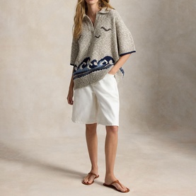 Model wearing Polo Ralph Lauren cream knit poncho with navy wave border, styled with white shorts and tan sandals