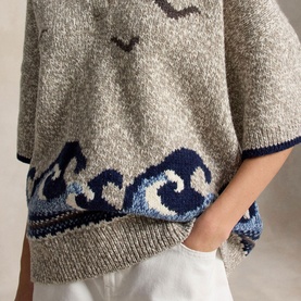 Model wearing Polo Ralph Lauren cream knit with navy wave and seagull intarsia pattern, short sleeves, styled with white trousers.