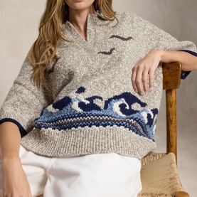 Model wearing Polo Ralph Lauren cream knit sweater with navy wave and seagull intarsia pattern, quarter-zip collar, styled with white trousers
