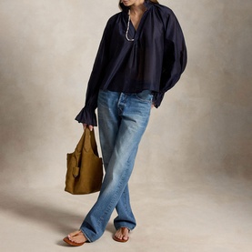 Model wearing Polo Ralph Lauren Trapeze Ruffle Blouse in Hunter Navy with blue jeans, styled with an olive tote bag and tan sandals.