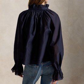 Model wearing Polo Ralph Lauren Hunter Navy shirt with ruffle high neck and flared cuffs, styled with blue jeans, back view.