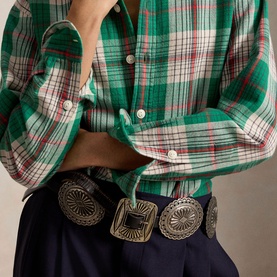 Model wearing Polo Ralph Lauren green and cream plaid shirt, sleeves rolled, styled with a silver concho belt and navy trousers.