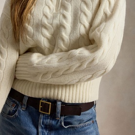 Model wearing Polo Ralph Lauren Authentic Cream cable-knit sweater, styled with blue denim jeans and a dark brown leather belt.