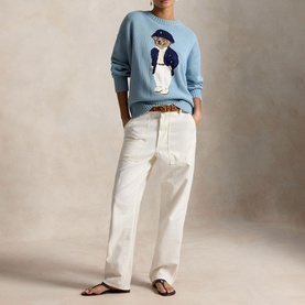 Model wearing Polo Ralph Lauren Blue Note knit jumper with Polo Bear motif, styled with white wide-leg trousers and brown belt.