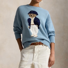 Model wearing Polo Ralph Lauren Blue Note knit sweater with intarsia Polo Bear motif, styled with white jeans and leopard-print belt